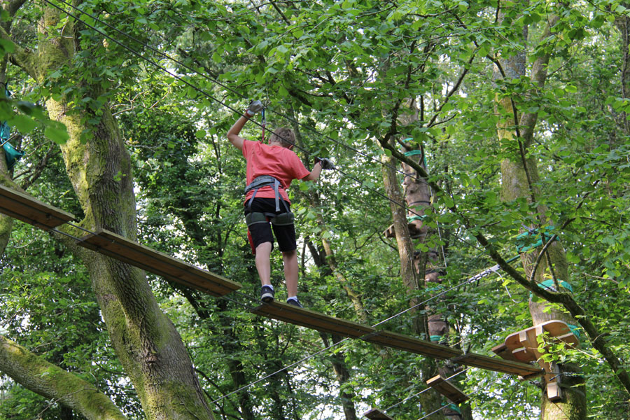 Vue sur un enfant qui traverse des planches suspendues dans l'accrobranche du Finistère Adrénature Parc Aventure ©office du tourisme de quimper