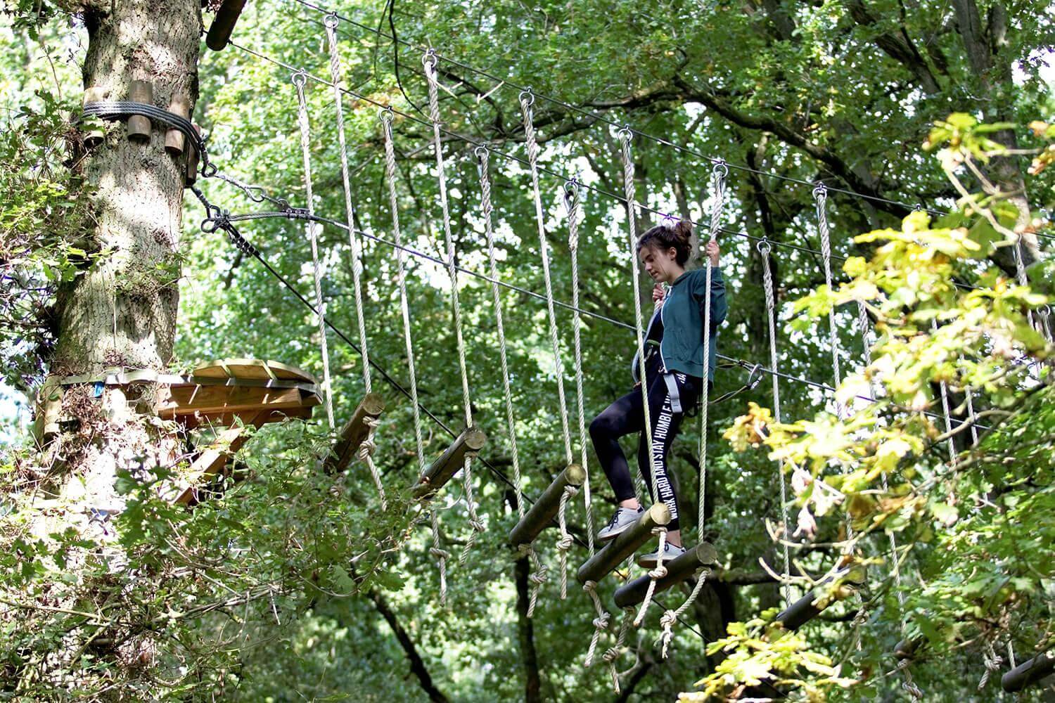 Une jeune utilisatrice traverse le chemin des rondins suspendus dans le parc Arbr'en Ciel ©Arbr'en Ciel